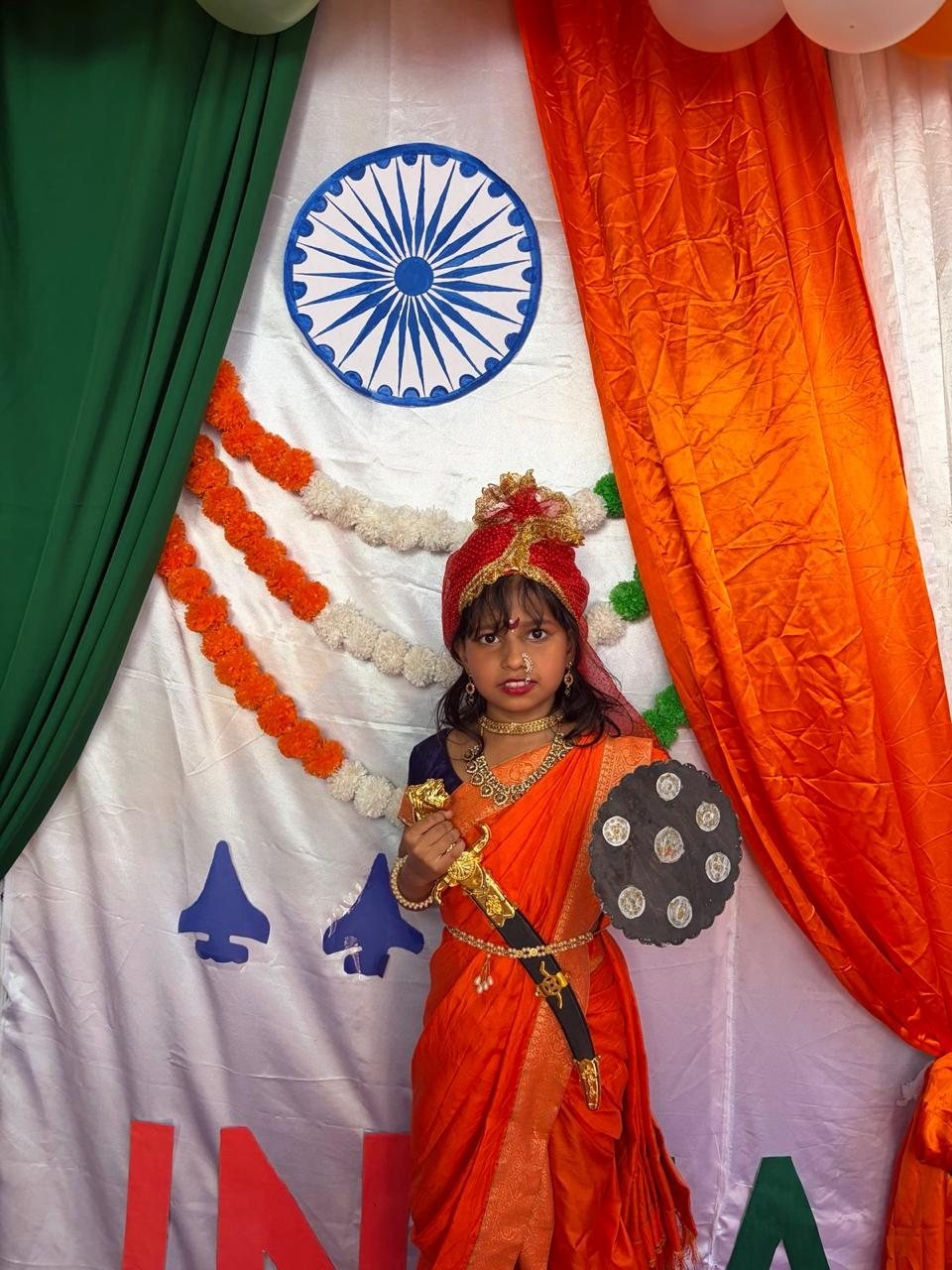 Student dressed as a warrior queen in front of the tricolour backdrop